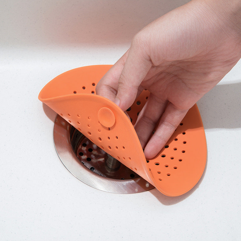 Hand holding an orange sink floor drain over a stainless steel sink drain opening.