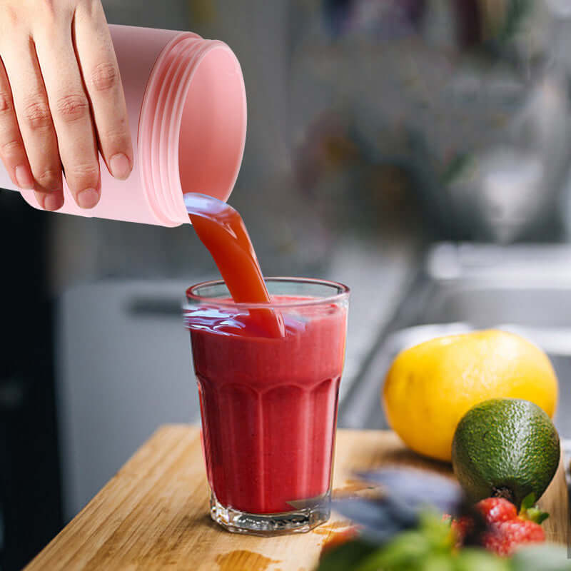 Hand pouring smoothie from a mini portable blender for smoothies into a glass on a wooden surface.