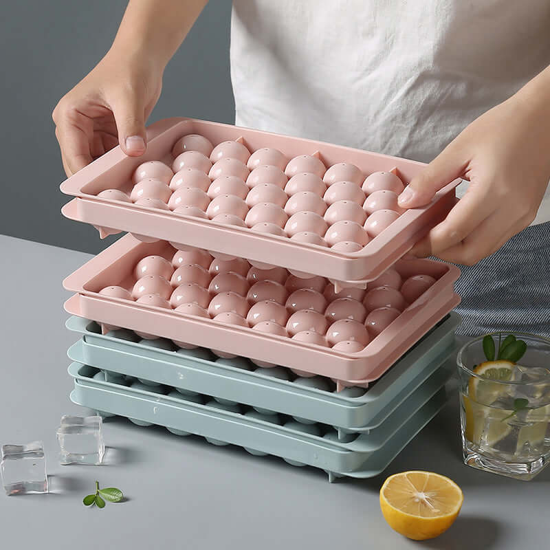 3D round ice cube mold for drinks, user handling pink and blue ice cube trays with ice cubes.