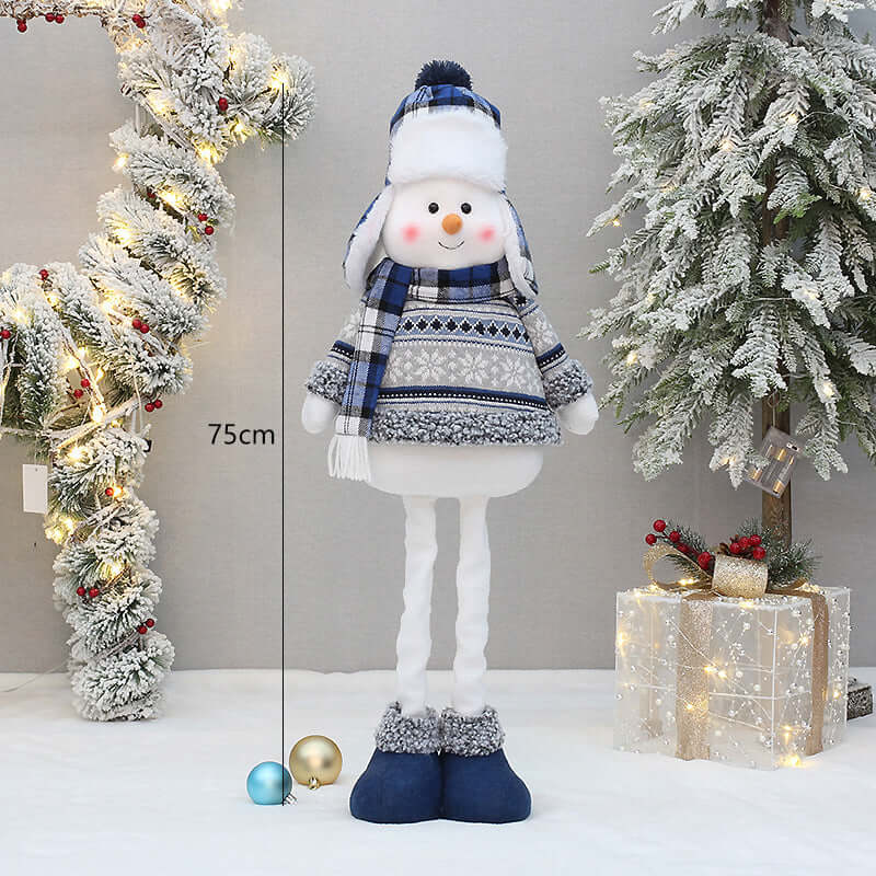 Christmas New Product Blue Fabric Expandable Snowman Doll Adornment Decoration standing beside a decorated Christmas tree.
