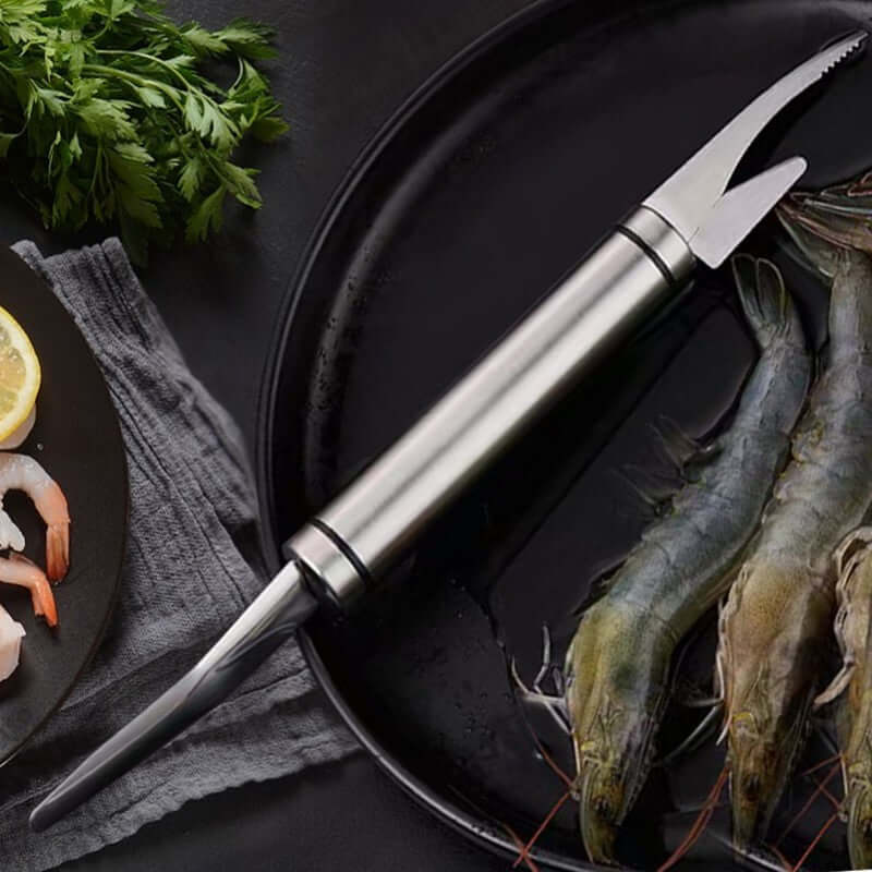 Multifunction Stainless Steel Shrimp Deveiner & Fish Scale Remover Tool on a black plate with fresh shrimp and herbs.